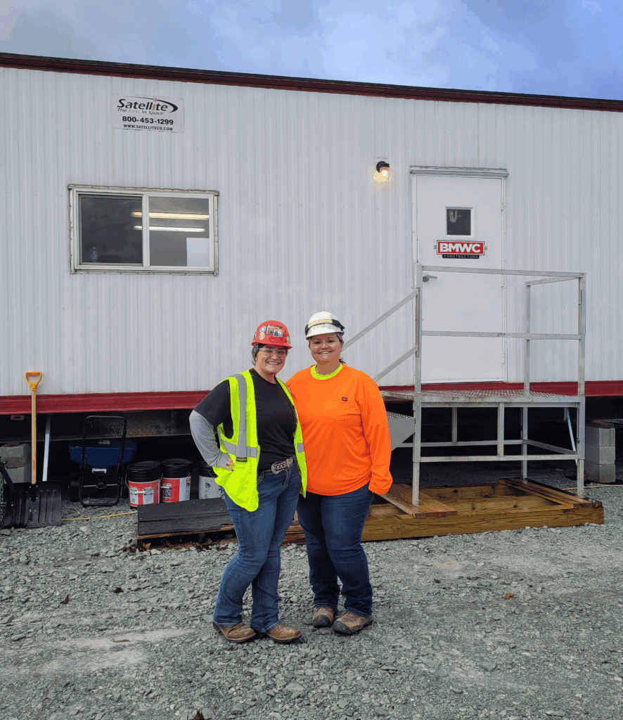 Women in construction workwear standing in front of jobsite trailer representing minority